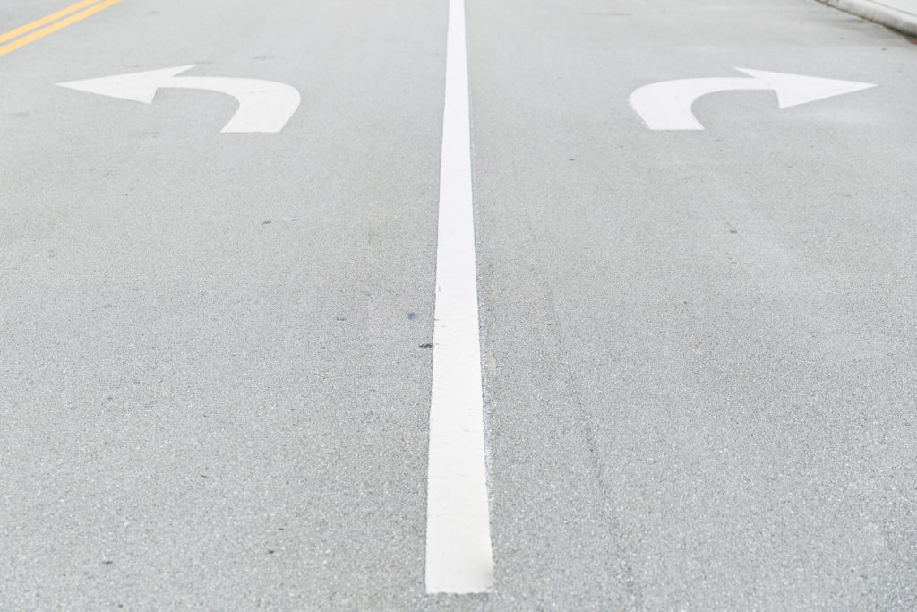 White arrow signs painted on road as direction restriction. Arrow signs as road markings on a street with two lanes